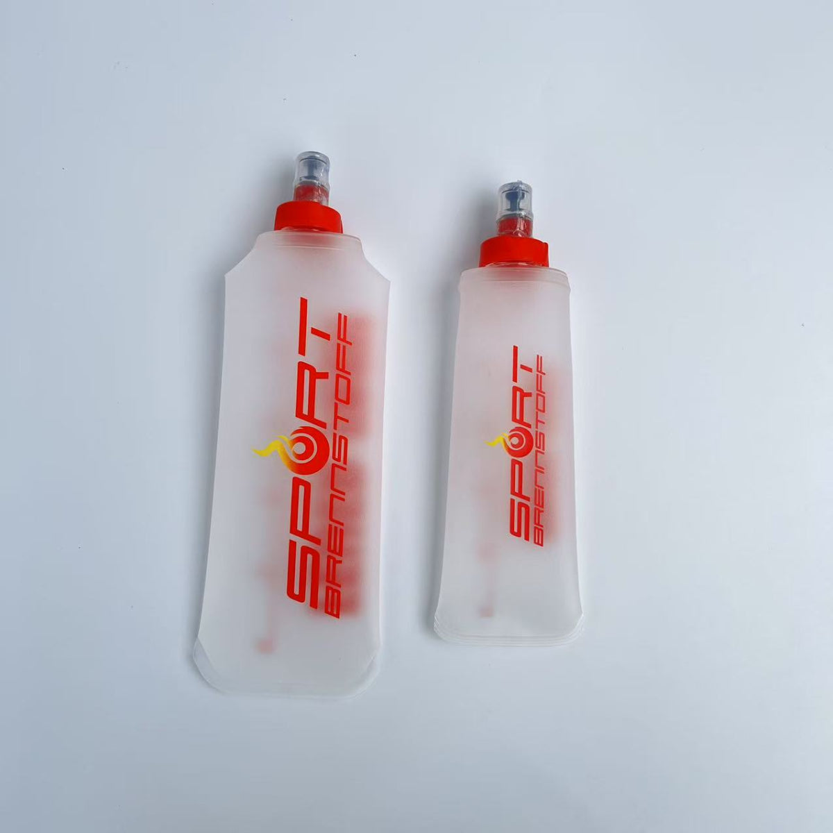 SportBrennstoff BEGLEITER - Trinkflasche in zwei Größen mit rotem Verschluss, flexibel und tropfsicher für Outdoor-Aktivitäten wie Laufen und Radfahren.