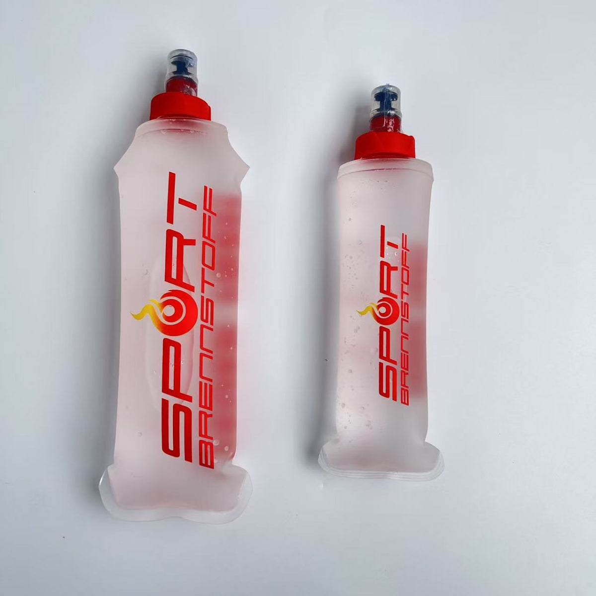 SportBrennstoff BEGLEITER - Trinkflasche in zwei Größen mit rotem Verschluss, flexibel und tropfsicher für Outdoor-Aktivitäten.