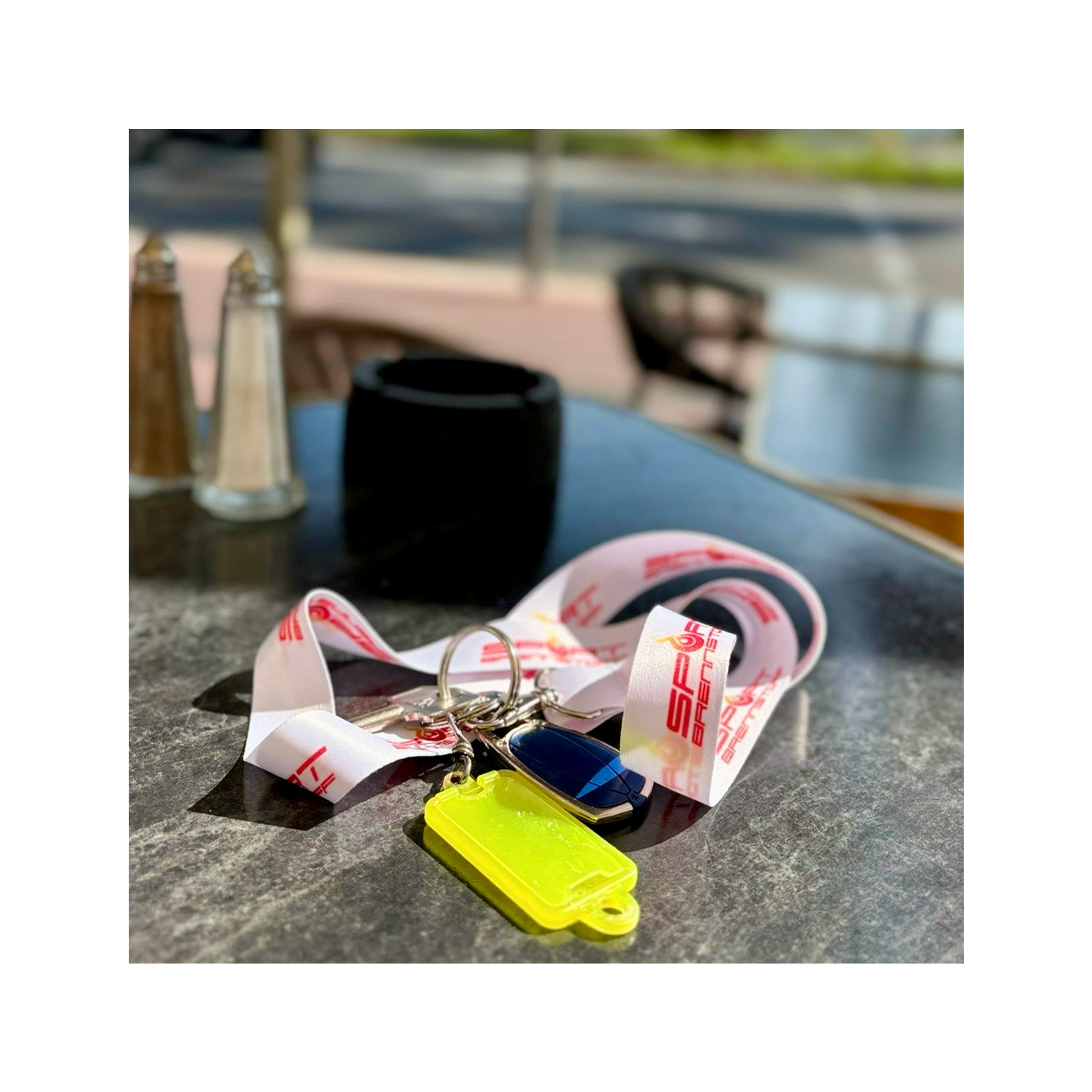 SportBrennstoff Schlüsselband / Lanyard für einen besonderen Auftritt mit Logo in Weiß-Rot, auf einem Tisch mit Schlüsseln und Anhängern platziert.