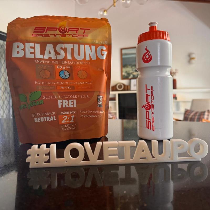 SportBrennstoff BELASTUNG Pulver für effizientes Training mit neutralem Geschmack und 2:1 Carb-Mix, neben Sporttrinkflasche im Wohnzimmer.